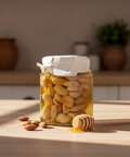 Jar of honey with almonds on a wooden table, with a honey dipper nearby.