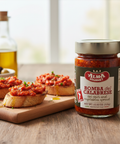 Jar of Alma Gourmet Bomba del Calabrese hot chili and vegetables spread on a wooden surface with bruschetta.