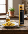 Pasta with truffle in a cylindrical container on a wooden table with a plate of pasta.