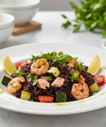 Plated dish of black rice with shrimp and vegetables on a white plate.