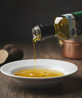 Bottle of olive oil being poured into a white bowl on a wooden surface.