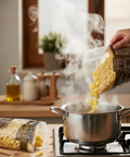 Person pouring popcorn kernels into a pot on a stove with steam rising.