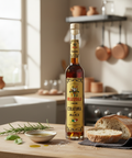 Bottle of Rizzoli Colatura d'Alici on a kitchen counter with bread and herbs.