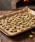 Sheet pan of baked mushrooms with herbs on a wooden surface, with a brick oven in the background.