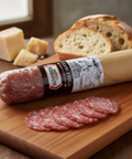 Packaged salami with slices on a wooden board, surrounded by bread and cheese.