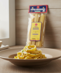 Pasta dish with a package of pasta in the background on a wooden table.
