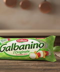 Packaged product labeled 'Galbanino' on a wooden table with bread and tomatoes in the background.
