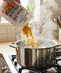 Pasta being poured into a pot of boiling water on a stove with steam rising.