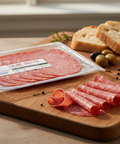 Packaged salami on a wooden cutting board with bread and cheese.