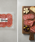 Packaged salami next to a wooden board with sliced salami, cheese, and olives.
