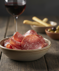 Bowl of salami with a glass of red wine on a wooden table