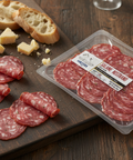Packaged salami slices on a wooden board with cheese and bread