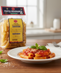 Pasta dish with penne pasta on a plate, basil leaves, and a package of Pastai Gragnanesi in the background.