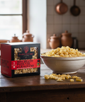 Box of pasta and bowl of pasta on a wooden table in a kitchen setting