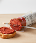 Tube of red spreadable food being used to spread on a piece of bread.