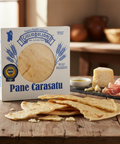 Box of Giulio Bulloni Pane Carasatu with flatbread on a wooden surface