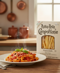 Pappardelle pasta with tomato sauce on a plate next to a box of Antica Pasta di Campofilone in a kitchen setting.