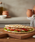 Grilled sandwich with lettuce and tomato on a wooden cutting board in a kitchen setting.