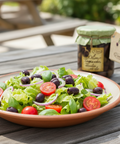 Salad with olives and tomatoes on a wooden table with a jar of olive oil in the background.