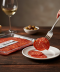 Person picking up a salami slice from a plate with a glass of white wine and Parmesan cheese in the background.