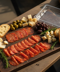Wooden charcuterie board with sliced salami, cheese, olives, and bread on a wooden surface.