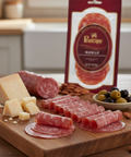 Wooden cutting board with sliced salami, cheese, and olives, featuring a Principe Salame package.