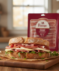 Sandwich with deli meats on a wooden cutting board with a package of deli meat in the background.
