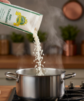 Rice being poured from a package into a pot on a stove with steam rising.