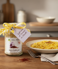 Jar of saffron with a label next to a bowl of risotto on a wooden table.