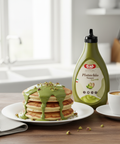 Pistachio syrup bottle next to pancakes with syrup on a kitchen counter