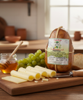 Provolone cheese with honey, grapes, and bread on a wooden board in a kitchen setting.