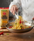 Chef cooking spaghetti with tomatoes in a pan next to a package of Spaghetto Italiano pasta.