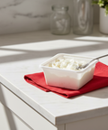 Container of food on a red napkin with a spoon on a white surface