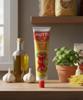 Mutti tomato paste tube on a kitchen counter with pasta and ingredients in the background