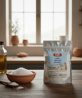 Alma Fine Trapani Sea Salt packaging on a wooden table with a bowl of salt and olive oil bottles.
