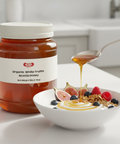 Jar of organic white truffle acacia honey with a spoon drizzling honey over a bowl of cereal with fruit.