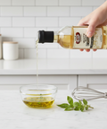 Person pouring white wine vinegar from a bottle into a glass bowl on a kitchen counter.