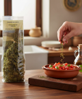 Hand sprinkling herbs from a package next to a bowl of salad on a wooden table.