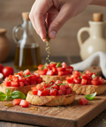 Hand sprinkling herbs over bruschetta on a wooden board with olive oil and tomatoes in the background.